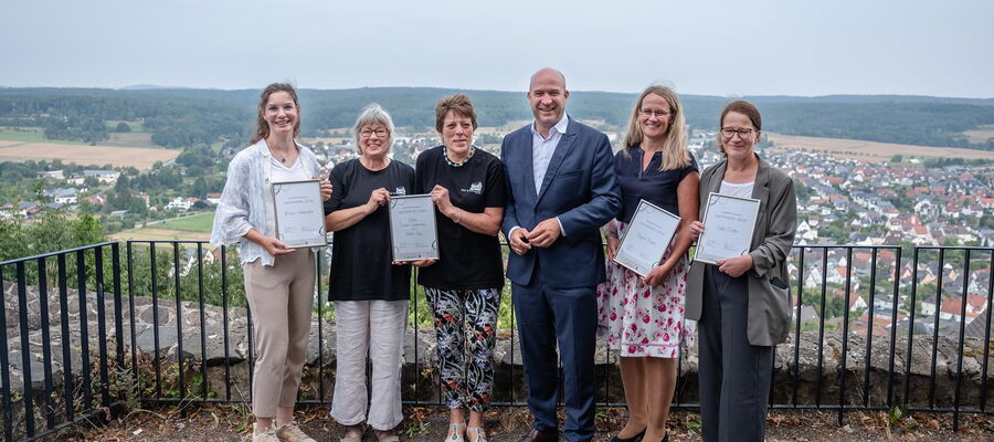 Die Preistragenden des Preis LandHeldin stehen an der Burgmauer der Burg Gleiberg zusammen mit Heimatminister Ingmar Jung und halten gemeinsam ihre Urkunden hoch.