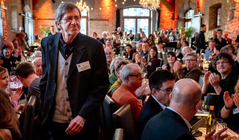 Der Preisträger Willi Schmidt ist auf dem Weg zur Bühne und geht dazu durch eine Reihe Beifall klatschenden Gäste.