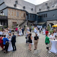Die Gäste der Sommergala zum Preis LandHeldin stehen verteilt auf dem Burghof der Burg Gleiberg und sprechen miteinander.