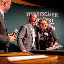 Die beiden Preistragenden vom Verein Dialekt im Hinterland e.V. stehen, zusammen mit Heimatminister Ingmar Jung, auf einer Bühne und freuen sich über die Auszeichnung.