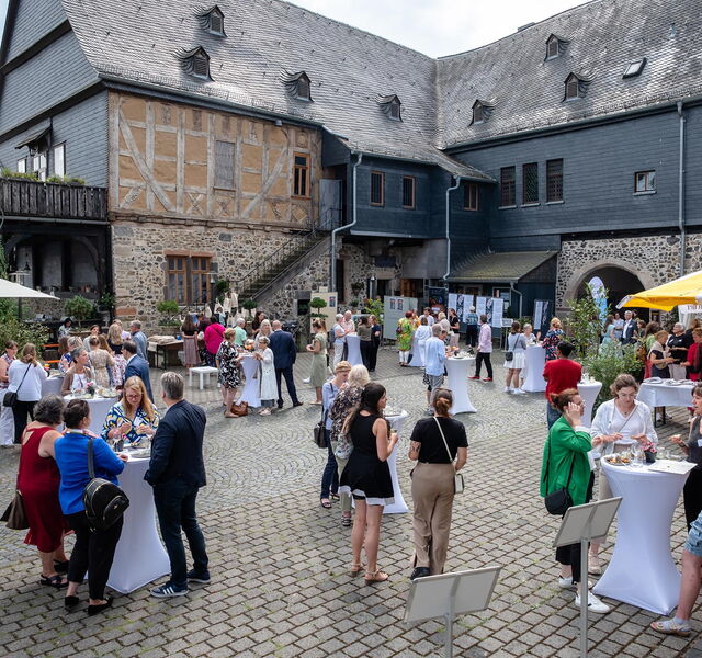 Die Gäste der Sommergala zum Preis LandHeldin stehen verteilt auf dem Burghof der Burg Gleiberg und sprechen miteinander.