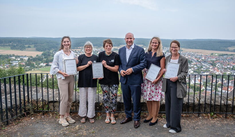 Die Preistragenden des Preis LandHeldin stehen an der Burgmauer der Burg Gleiberg zusammen mit Heimatminister Ingmar Jung und halten gemeinsam ihre Urkunden hoch.