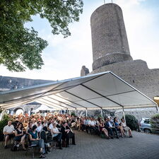 Viele Menschen sitzen bei Sonnenschein auf dem Burghof der Burg Gleiberg und lauschen der Preisverleihung der LandHeldin.